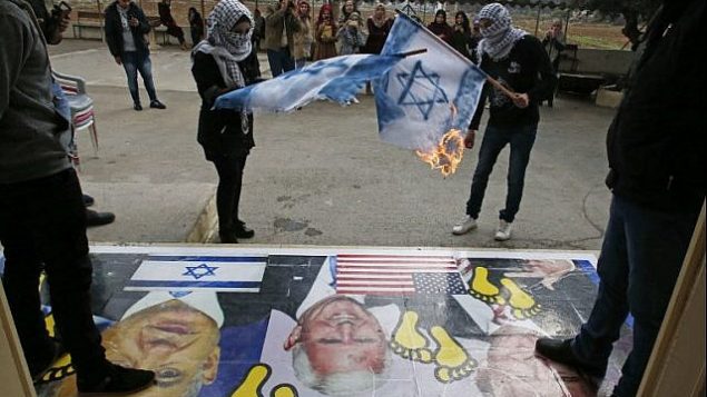 يحرق الفلسطينيون أعلام إسرائيلية بجوار ملصق يحمل صورا للرئيس الأمريكي دونالد ترامب ونائبه مايك بينس ورئيس الوزراء الإسرائيلي بنيامين نتنياهو خلال مظاهرة في جامعة القدس المفتوحة في قرية دورا في ضواحي مدينة الخليل بالضفة الغربية في 13 ديسمبر 2017. (AFP Photo/Hazem Bader)