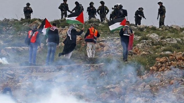 رجال فلسطينيون يرفعون الأعلام أمام القوات الإسرائيلية خلال مظاهرة تخلد ذكرى يوم الأرض في قرية كسرى بالضفة الغربية في 30 مارس / آذار 2018. (AFP/Jaafar Ashtiyeh)