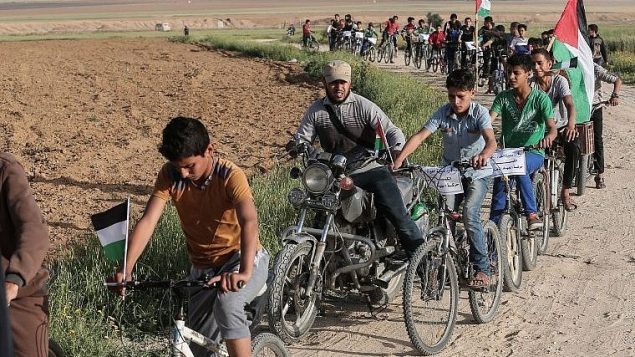 اطفال فلسطينيون يركبون دراجات هوائية بالقرب من الحدود الإسرائيلية في ضواحي خان يونس، جنوب قطاع غزة، خلال سباق دراجات يطالب ’بحق عودة’ ملايين اللاجئين الفلسطينيين الى اسرائيل، 26 مارس 2018 (AFP/Said Khatib)