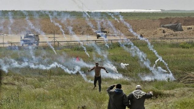صورة تم التقاطها في 30 مارس، 2018 تظهر فلسطينيين يفرون من قنابل الغاز المسيل للدموع خلال تظاهرة بالقرب من السياج الحدودي مع إسرائيل، شرقي مدينة غزة. (AFP/Mahmud Hams)
