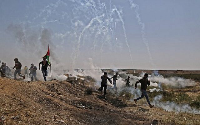 رجال فلسطينيون يهرعون للحماية من عبوات الغاز المسيل للدموع على الحدود بين إسرائيل وغزة خلال مظاهرة، شرق مدينة غزة في قطاع غزة، في 6 أبريل 2018. (AFP PHOTO / MAHMUD HAMS)