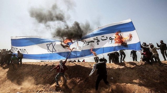 متظاهرون فلسطينيون يحرقون علما إسرائيليا خلال مواجهات مع قوى الأمن الإسرائيلية عند السياج الحدودي بين غزة وإسرائيل، شرقي خان يونس، في شمال قطاع غزة، 8 أبريل، 2018. (AFP PHOTO / SAID KHATIB)