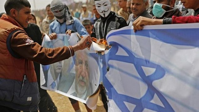فلسطينيون يستعدون لإشعال النيران بعلم إسرائيل وصور لوزير الدفاع أفيغدور ليبرمان ورئيس الوزراء بنيامين نتنياهو خلال احتجاج على السياج الحدودي مع إسرائيل، شرق خان يونس في جنوب مدينة غزة، في 13 أبريل  2018. (AFP/Thomas Coex)