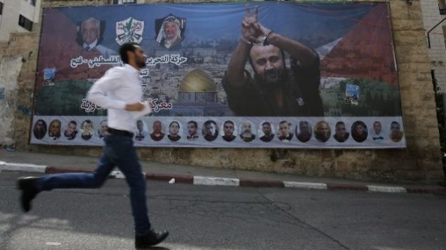 فلسطيني يمر من أمام ملصق يحمل صورة للقيادي والأسير الفلسطيني مروان البرغوثي في مدينة رام الله في الضفة الغربية، 3 مايو، 2017.  (AFP/ ABBAS MOMANI)
