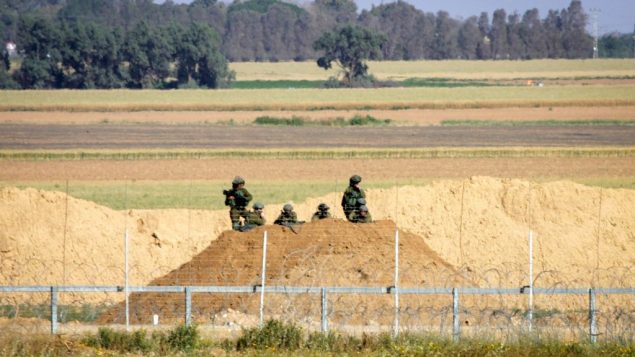 جنود إسرائيليون يراقبون محتجين فلسطينيين في أعقاب مظاهرة بالقرب من السياج الحدودي مع إسرائيل، شرقي خان يونس، في جنوب قطاع غزة، 1 أبريل، 2018. (Abed Rahim Khatib/ Flash90)