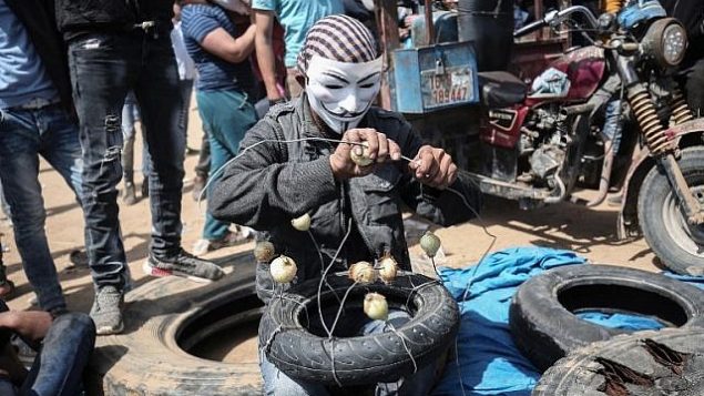 رجل فلسطيني مقنع يتهيأ للتظاهر مع بصل، الذي يهدف تخفيف تأثير الغاز المسيل للدموع بالقرب من خان يونس، شرقي مدينة غزة، 6 ابريل 2018 (SAID KHATIB / AFP)