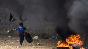 متظاهر فلسطيني يركض وهو يحمل إطاراً لإطلاق النار أثناء الاشتباكات مع القوات الإسرائيلية على طول الشريط الحدودي مع قطاع غزة شرق مدينة غزة في 4 أيار / مايو 2018. (AFP PHOTO / MAHMUD HAMS)