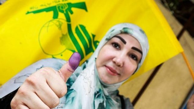 امراة شيعية لبنانية تعرض ابهامها الملون بالحبر وتلوح بعلم حزب الله بعد التصويت في محطة اقتراع في العاصمة بيروت في 6 مايو، 2018، في اليوم الذي تجري فيه البلاد انتخابات برلمانية لأول مرة منذ تسع سنوات. (AFP PHOTO / ANWAR AMRO)