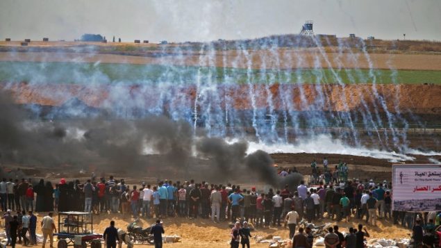 متظاهرون فلسطينيون ينظرون إلى الغاز المسيل للدموع والدخان المتصاعد من إطارات محترقة، شرقي مدينة غزة في 14 مايو، 2018 (AFP PHOTO / Mohammed ABED)