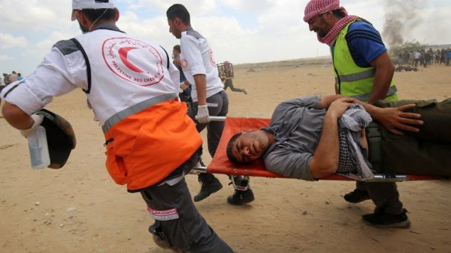 فلسطينيون يحملون متظاهرا مصابا خلال موجهات مع القوات الإسرائيلية عند الحدود بين قطاع غزة وإسرائيل، شرقي مدينة خان يونس، 14 مايو، 2018. ( AFP PHOTO / SAID KHATIB)