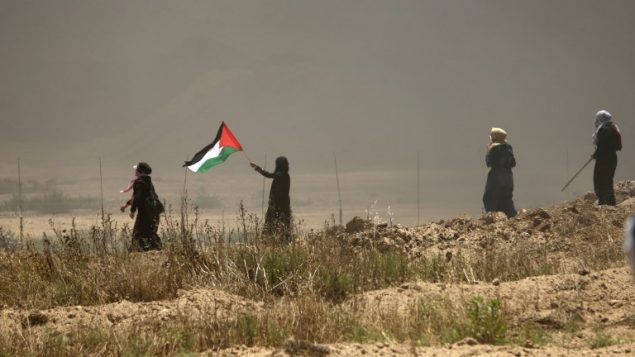 نساء فلسطينيات يوحن بالعلم الفلسطيني خلال مواجهات مع القوات الإسرائيلية بالقرب من الحدود بين قطاع غزة وإسرائيل، شرقي مدينة غزة، 14 مايو، 2018.  (AFP PHOTO / MAHMUD HAMS)