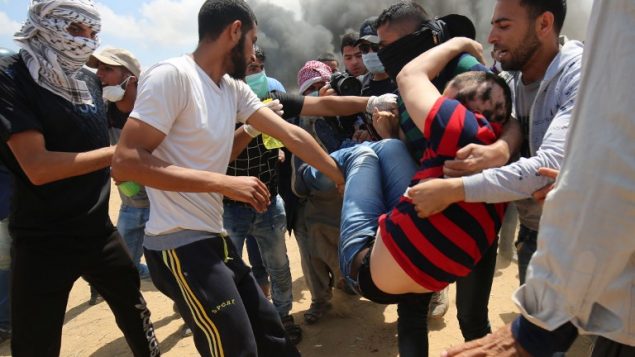 فلسطينيون يحملون متظاهرا مصابا خلال موجهات مع القوات الإسرائيلية عند الحدود بين قطاع غزة وإسرائيل، شرقي مدينة خان يونس، 14 مايو، 2018. ( AFP PHOTO / SAID KHATIB)