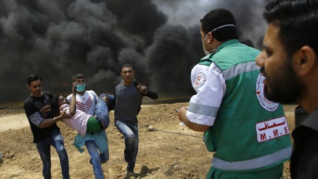 فلسطينيون يحملون متظاهراً أصيب خلال اشتباكات مع الجيش الإسرائيلي بالقرب من الحدود بين قطاع غزة وإسرائيل  14 مايو / أيار 2018 يوم تدشين السفارة الأمريكية في القدس MAHMUD HAMS / AFP