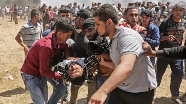 فلسطينيون يحملون متظاهراً أصيب خلال اشتباكات مع الجيش الإسرائيلي بالقرب من الحدود بين قطاع غزة وإسرائيل  14 مايو / أيار 2018 يوم تدشين السفارة الأمريكية في القدس (MAHMUD HAMS / AFP)