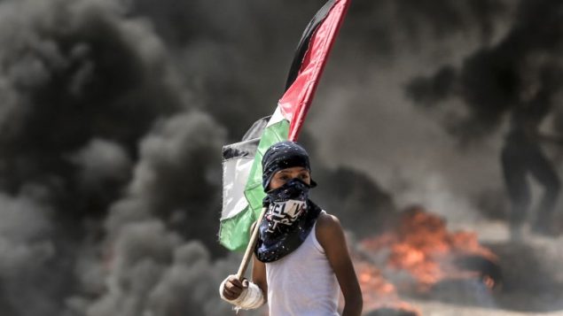 فتى من غزة يحمل العلم الفلسطيني  خلال اشتباكات مع الجيش الإسرائيلي بالقرب من الحدود بين قطاع غزة وإسرائيل  14 مايو / أيار 2018 يوم تدشين السفارة الأمريكية في القدس MAHMUD HAMS / AFP
