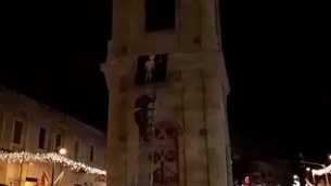 ناشطان من منظمة ’عوتسما يهوديت’ يقومون بتعليق صورة لمنفذ هجوم على برج الساعة في يافا.  (لقطة شاشة: Ynet news)