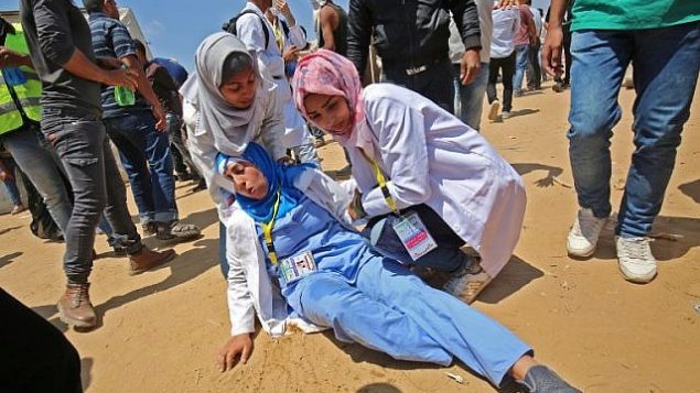 رزان النجار (من اليمين)، مسعفة فلسطينية تبلغ من العمر 21 عاما تقدم الإسعاف لإحدى زميلاتها التي أصيبت خلال مواجهات بالقرب من الحدود مع إسرائيل، شرقي خان يونس في جنوب قطاع غزة، 15 مايو، 2018.  (AFP/ SAID KHATIB)