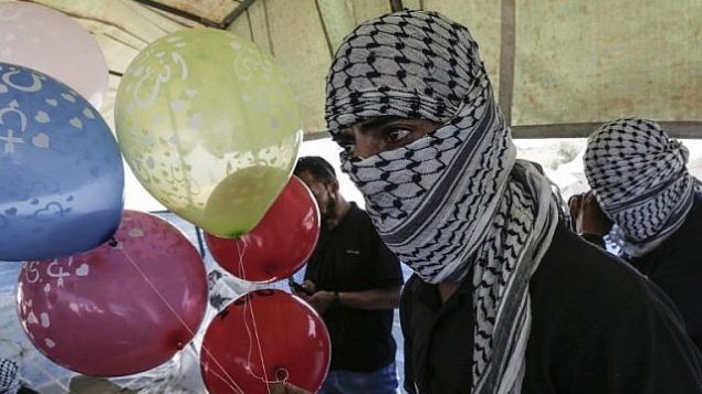 محتجون فلسطينيون يعدون بالونات محملة بمواد حارقة لإطلاقها باتجاه إسرائيل، عند حدود غزة إسرائيل في البريج، وسط قطاع غزة، 14 يونيو، 2018.  (AFP/Mahmud Hams)