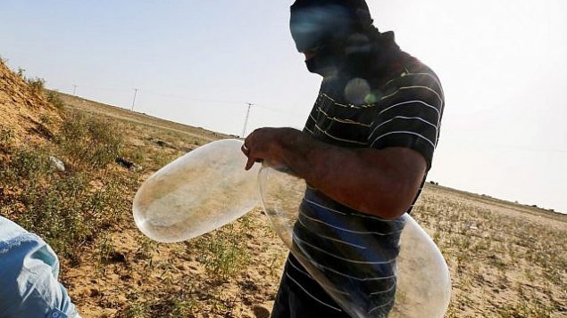 ملثم فلسطيني يعد بالونا سيقوم تحميله بمواد حارقة لإطلاقه باتجاه إسرائيل بالقرب من الحدود الإسرائيلية مع غزة، في مدينة رفح بجنوب قطاع غزة، 17 يونيو، 2018.  (Abed Rahim Khatib/Flash90)