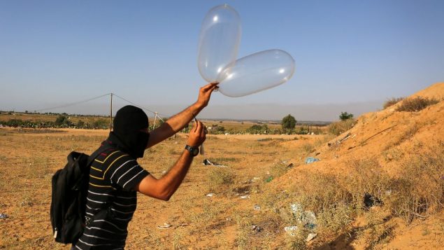 ملثم فلسطيني يطلق بالونا محملا بمواد حارقة باتجاه إسرائيل من مدينة رفح في جنوب قطاع غزة في 17 يونيو، 2018 (Abed Rahim Khatib/Flash90)