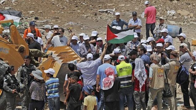 يرفع المتظاهرون الأعلام الفلسطينية وهم يحاولون منع جرافات من فتح طريق وصول إلى قرية الخان الأحمر البدوية في الضفة الغربية في 4 يوليو 2018. (AFP Photo/Ahmad Gharabli)