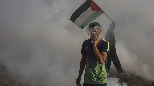 قنابل غاز مسيل للدموع القاها جنود اسرائيليين تتساقط بين فلسطينيين يتظاهروا عند حدود قطاع غزة، 13 يوليو 2018 (Wissam Nassar/Flash90)