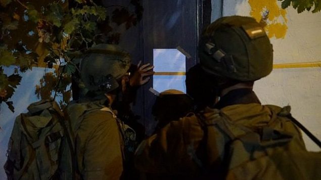 جنود إسرائيليون يعلقون إخطار هدم على منزل منفذ هجوم فلسطيني من قرية كوبر الفلسطينية في الضفة الغربية قام قتل إسرائيلي طعنا في الشهر الماضي، 13 أغسطس، 2018. (الجيش الإسرائيلي)