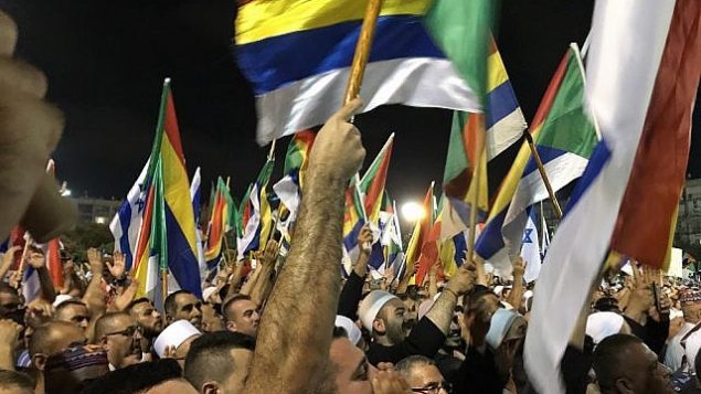 متظاهرون يلوحون بالأعلام الإسرائيلية والدرزية خلال مظاهرة في تل ابيب ضد قانون الدولة اليهودية، 4 اغسطس 2018 (Luke Tress / Times of Israel staff)