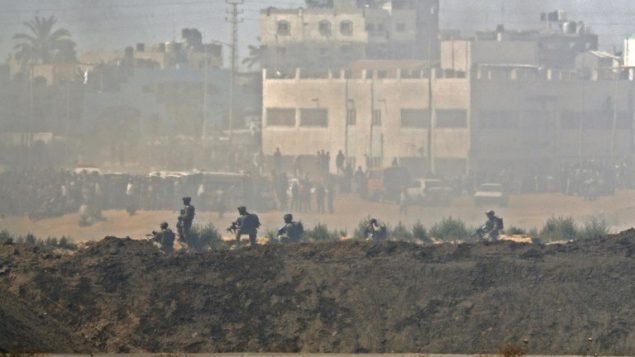 صورة تم التقاطها في 14 مايو، 2018 من كيبوتس ناحال عوز في جنوبي إسرائيل عبر الحدود مع غزة لجنود إسرائيليين ومتظاهرين فلسطينيين يحتشدون بالقرب من السياج الحدودي مع إسرائيل. (AFP/JACK GUEZ) صورة تم التقاطها في 14 مايو، 2018 من كيبوتس ناحال عوز في جنوبي إسرائيل عبر الحدود مع غزة لجنود إسرائيليين ومتظاهرين فلسطينيين يحتشدون بالقرب من السياج الحدودي مع إسرائيل. (AFP/JACK GUEZ)