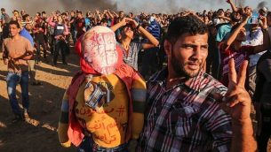 أحد المتظاهرين الفلسطينيين يلمح ببادرة النصر بينما يمسك دمية ترتدي قناعًا يصور وجه الرئيس الأمريكي دونالد ترامب مغطى بالدماء وقميصًا يحمل شعارًا عربيًا "مستمرون رغم أنف ترامب" ، أثناء مظاهرة على الحدود بين إسرائيل وغزة، شرق مدينة غزة في وسط القطاع في 7 سبتمبر 2018. (AFP/Said Khatib)