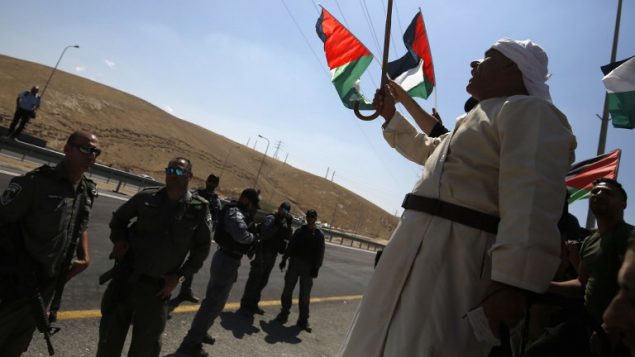 متظاهرون فلسطينيون يلوحون بالاعلام الوطنية امام جنود اسرائيليين خلال مظاهرة ضد هدم قرية خان الاحمر البدوية في الضفة الغربية، 14 سبتمبر 2018 (AFP PHOTO / ABBAS MOMANI)