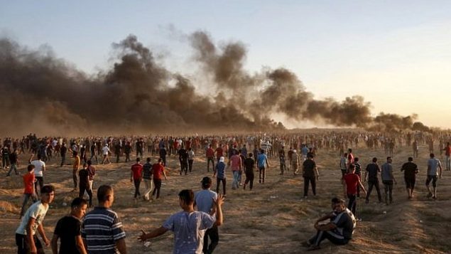 متظاهرون فلسطينيون يجتمعون أثناء مظاهرة على امتداد السياج الحدودي الإسرائيلي شرق مدينة غزة في 21 سبتمبر 2018 حيث تتصاعد أعمدة الدخان من الإطارات المحترقة في الخلفية. (AFP/Said Khatib)