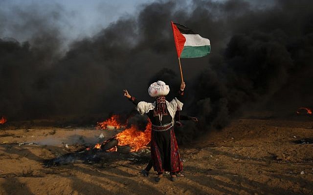 امرأة فلسطينية ترفع العلم أمام إطارات محترقة خلال اشتباكات على طول السياج الحدودي، شرق مدينة غزة في 28 سبتمبر 2018. ( AFP PHOTO / Said KHATIB) امرأة فلسطينية ترفع العلم أمام إطارات محترقة خلال اشتباكات على طول السياج الحدودي، شرق مدينة غزة في 28 سبتمبر 2018. ( AFP PHOTO / Said KHATIB)