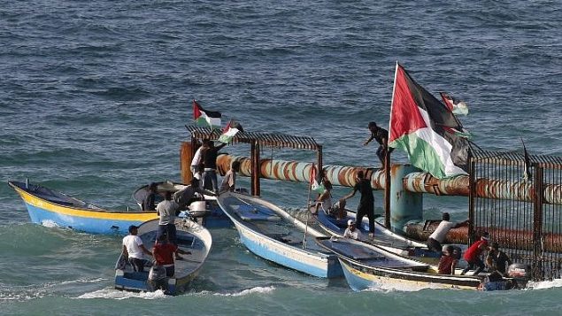 متظاهرون فلسطينيون على متن قوارب يرفعون الاعلام الفلسطينية على مبنى حديدي عند الحدود البحرية مع اسرائيل، في شمال قطاع غزة، 8 اكتوبر 2018 (AFP PHOTO / Said KHATIB)