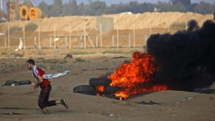 محتج فلسطيني يركض بجانب إطارات محترقة على الحدود بين إسرائيل وغزة، شرق مدينة غزة، في 12 أكتوبر 2018. (Said KHATIB / AFP)