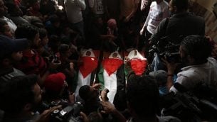 مشيعون يحملون جثامين ملفوفة بالأعلام الفلسطينية لثلاثية فتية قُتلوا في غارة جوية إسرائيلية، خلال جنازتهم في مدينة دير البلح، وسط قطا ع غزة، 29 أكتوبر، 2018. (MAHMUD HAMS / AFP)