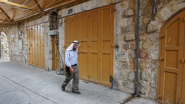 رجل فلسطيني يمر من أمام محلات تجارية مغلقة في البلدة القديمة في مدينة الخليل بعد الإعلان عن إضراب عام احتجاجا على قانون الدولة القومية الإسرائيلي، 1 أكتوبر، 2018.(Wisam Hashlamoun/Flash90)