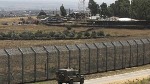 صورة تم التقاطها في 4 يوليو، 2018، من هضبة الجولان يظهر فيها نازحون سوريون من محافظة درعا (في أعلى الصورة من اليسار) يتظاهرون مطالبين المجتمع الدولي بالحماية، في قرية الرفيد السورية، بالقرب من السياج الحدودي مع إسرائيل. (AFP/Jalaa Marey)