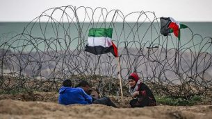 شبان فلسطينيون يجلسون بجانب علم فلسطيني بالقرب من السياج الشائك على طول الحدود مع إسرائيل شرق مدينة غزة أثناء تظاهرة حدودية في 7 ديسمبر/كانون الأول 2018. (Said Khatib/AFP)
