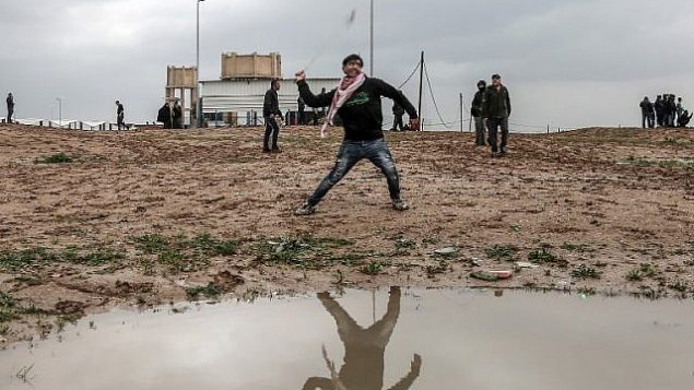 فلسطيني يقف بجوار مستنقع مياه أمطار بينما كان يستعمل مقلاعا لإلقاء جسم أثناء الاشتباكات مع القوات الإسرائيلية على طول الحدود، شرق مدينة غزة  في 28 ديسمبر / كانون الأول 2018. (Mahmud Hams/AFP)