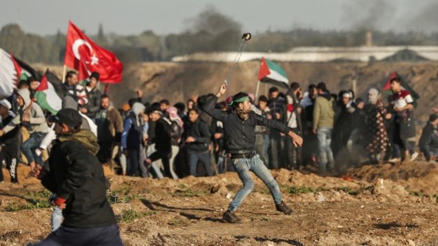متظاهر فلسطيني يستخدم مقلاع لرشق حجارة باتجاه القوات الإسرائيلية في الطرف الثاني من السياج الحدودي، خلال اشتباكات عند الحدود بين اسرائيل وقطاع غزة، 11 يناير 2019 (Mahmud Hams/AFP)