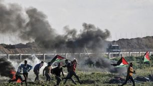 فلسطينيون يحملون الأعلام الفلسطينية يمرون من أمام إطارات محترقة خلال مواجهات بالقرب من السياج الحدودي مع إسرائيل، شرق مدينة غزة، 22 فبراير، 2019. (Mahmud Hams/AFP)