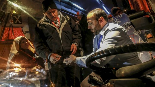 شرطي تابع لحركة حماس يفحص وثائق سفر معتمرين فلسطينيين يصعدون على متن حافلة في معبر رفح بين قطاع غزة ومصر، 3 مارس 2019 (SAID KHATIB / AFP)