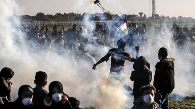 فلسطيني يستخدم مقلاعا لقذف عبوة الغاز المسيل للدموع التي ألقتها القوات الإسرائيلية خلال اشتباكات على السياج على طول الحدود مع إسرائيل، شرق مدينة غزة، في 8 مارس / آذار 2019. (Mahmud Hams/AFP)