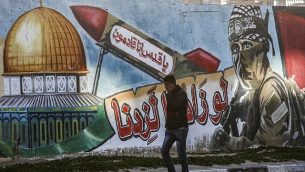 رجل فلسطيني يمر من أمام رسم لمقاتل ملثم من كتائب القسام، الجناح العسكري لحركة حماس، وإلى جانبه صاروخ تظهر عليه عبارة "يا قدس إنا قادمون" وقبة الصخرة، في أحد شوارع رفح في قطاع غزة، 14 مارس، 2019. (Photo by SAID KHATIB / AFP)