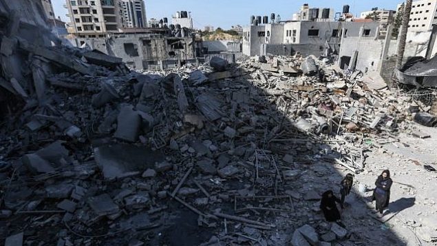 صورة تم التقاطها في 26 مارس، 2019، يظهر فيها فلسطينيون يقفون بالقرب من أنقاض أحد المباني في مدينة غزة، بعد أن استهدفت غارات جوية إسرائيلية عشرات المواقع في جميع أنحاء القطاع ليلا ردا على إطلاق صاروخ من القطاع الفلسطيني.  (MAHMUD HAMS / AFP)