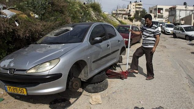 توضيحية: رجل فلسطيني يقوم بتغيير إطارات مركبته بعد هجوم ’تدفيع ثمن’ وقع في مارس 2014.  (photo credit: AFP/Ahmad Gharabli)