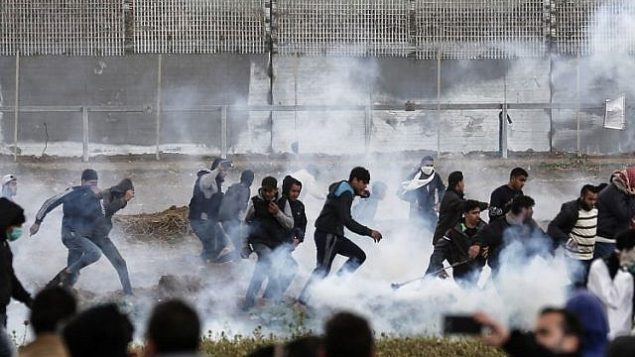 المتظاهرون الفلسطينيون يركضون للاحتماء من عبوات الغاز المسيل للدموع التي أطلقتها القوات الإسرائيلية خلال الاشتباكات وسط مظاهرة حاشدة احتفالا بالذكرى السنوية الأولى لاحتجاجات مسيرة العودة، بالقرب من الحدود مع إسرائيل شرق مدينة غزة في 30 مارس 2019. (Mahmud Hams/AFP)