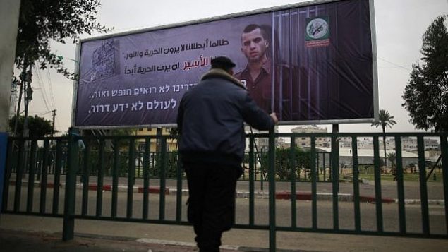 شرطي فلسطيني تابع لحركة "حماس" ينظر إلى لافتة تحمل صورة الجندي الإسرائيلي القتيل أورون شاؤول في مدينة غزة، 29 ديسمبر، 2017، كُتب عليها بالعربية: "طالما أبطالنا لا يرون الحرية والنور، هذا الأسير لن يرى الحرية أبدا".  (AFP PHOTO / MOHAMMED ABED)