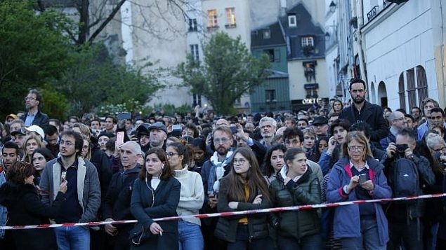 اشخاص يشاهدون الدخان والنيران تتصاعد من كاتدرائية نوتردام في باريس، 15 ابريل 2019 (AP/Michel Euler)